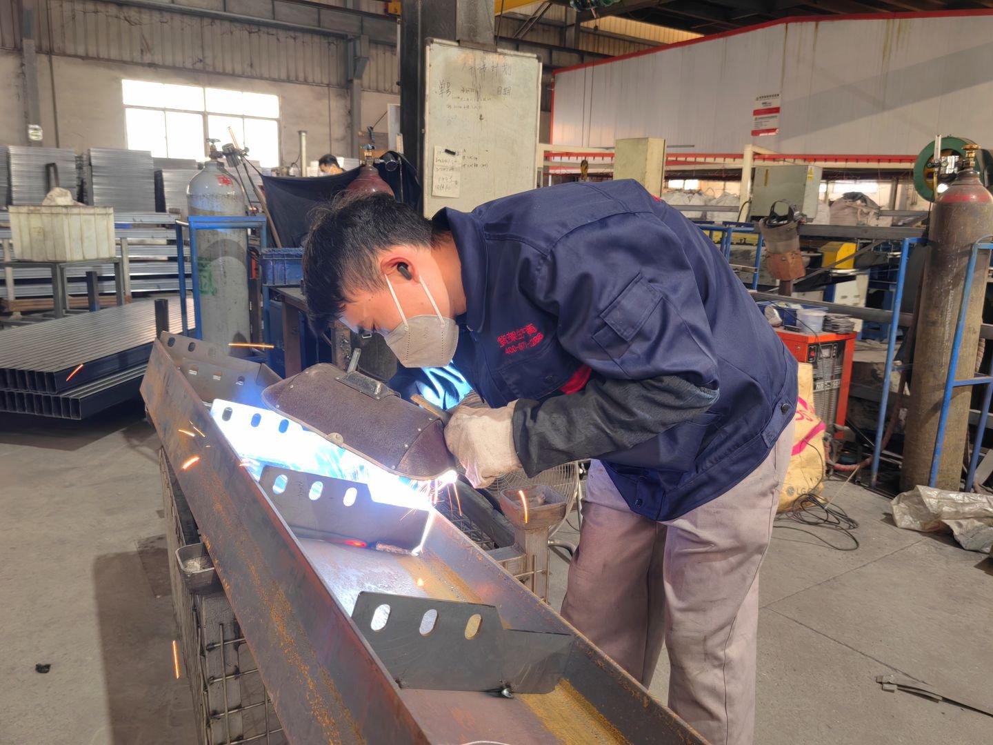 Welder joining a steel frame with a welding mask on